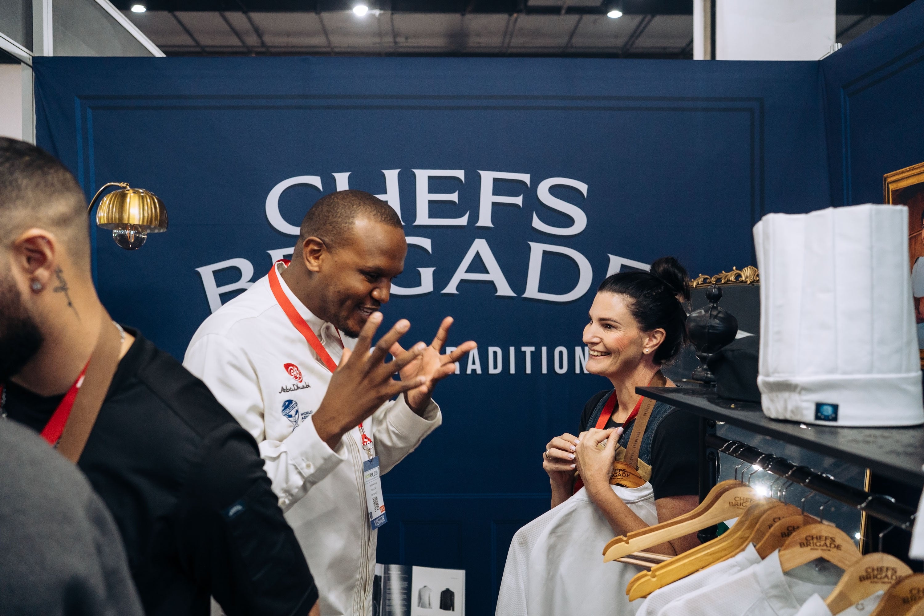Two chefs interacting in front of a 'Chefs Brigade' branded backdrop.