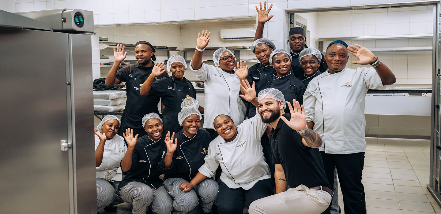 Group of chefs and kitchen staff posing for a photo in a professional kitchen.