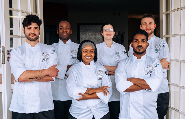 Group of chefs in white uniforms standing together outside a building.