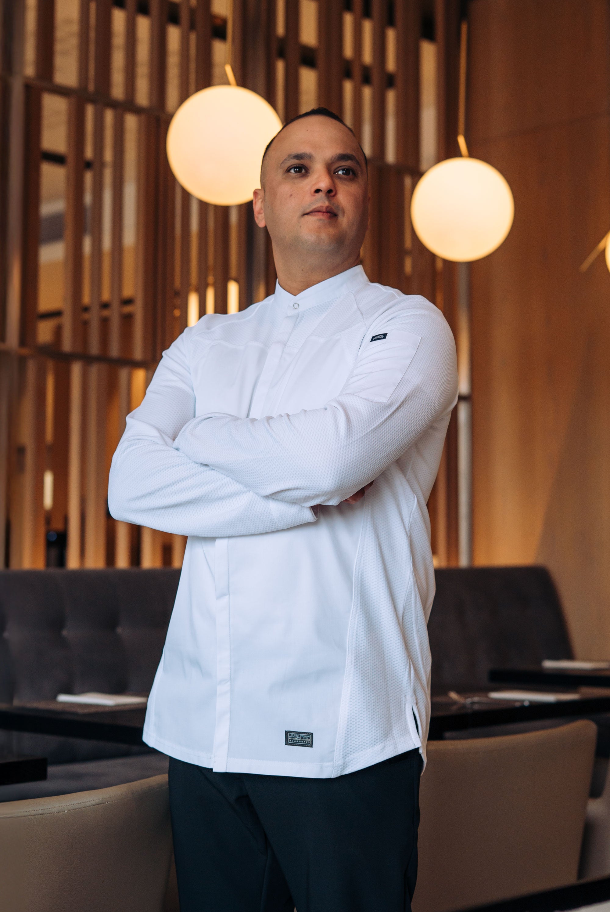 Man in a white chef's coat standing in a restaurant setting with warm lighting.