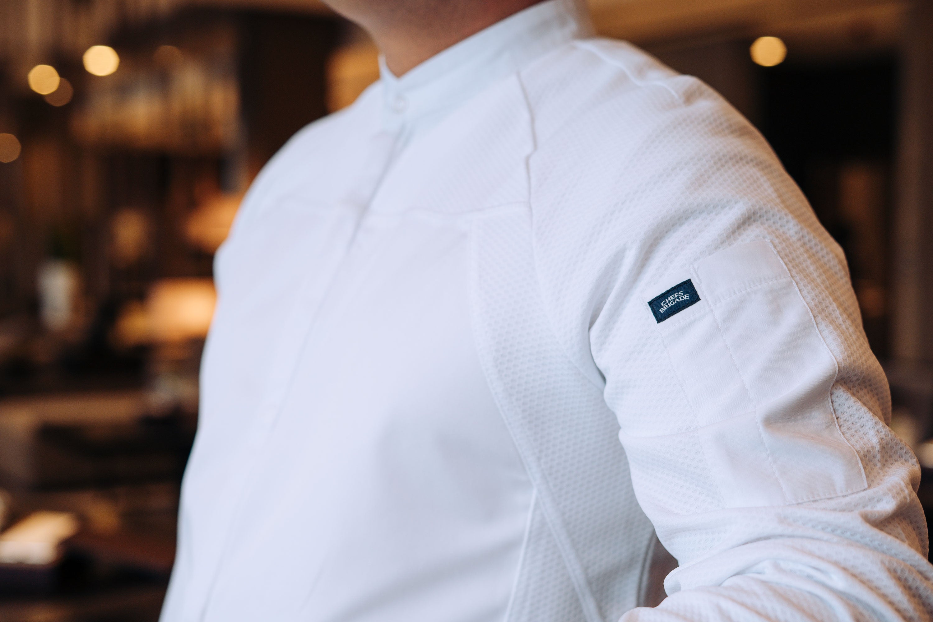 Person wearing a white chef shirt with the Chef Brigade logo in an indoor setting