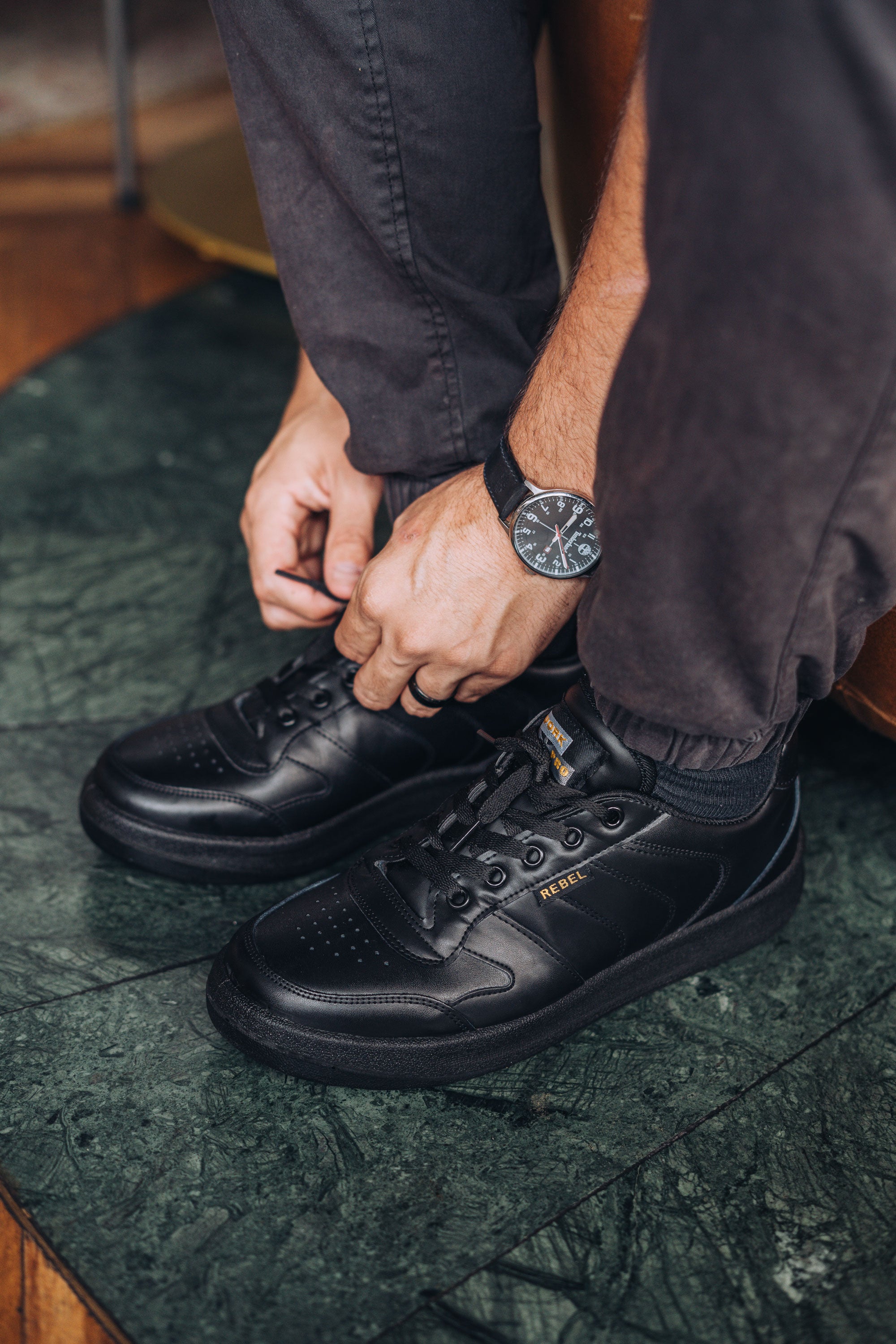 Person tying black chef shoes on a green textured floor